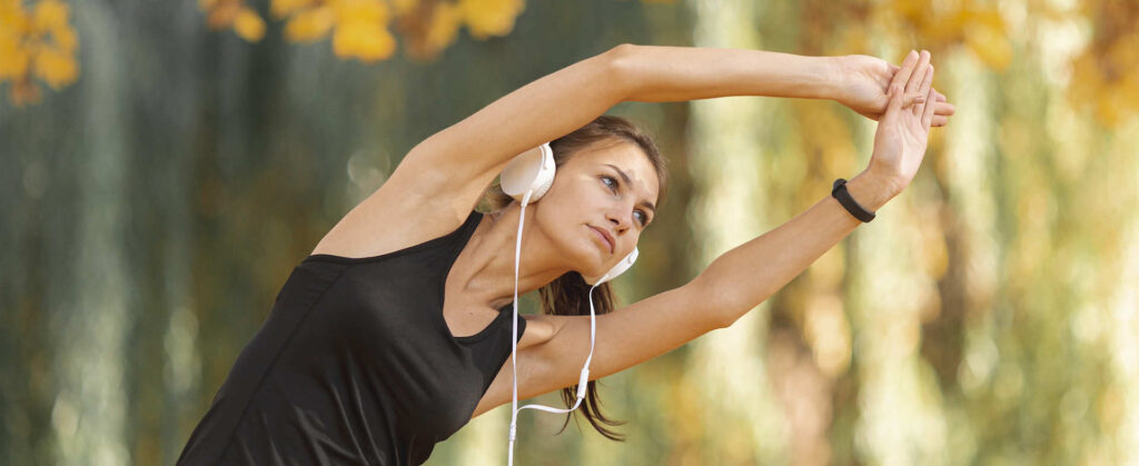 Mujer estirándose al aire libre mientras escucha música, promoviendo la actividad física para un estilo de vida saludable.