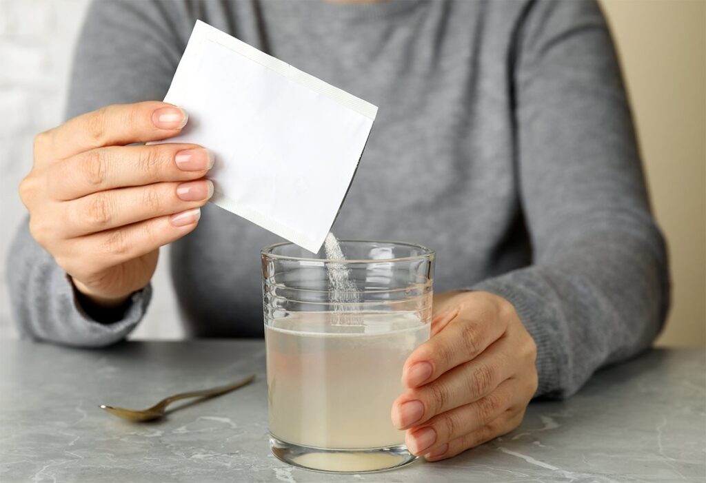 Persona preparando un suplemento de colágeno en un vaso de agua para el cuidado de la piel y las articulaciones.