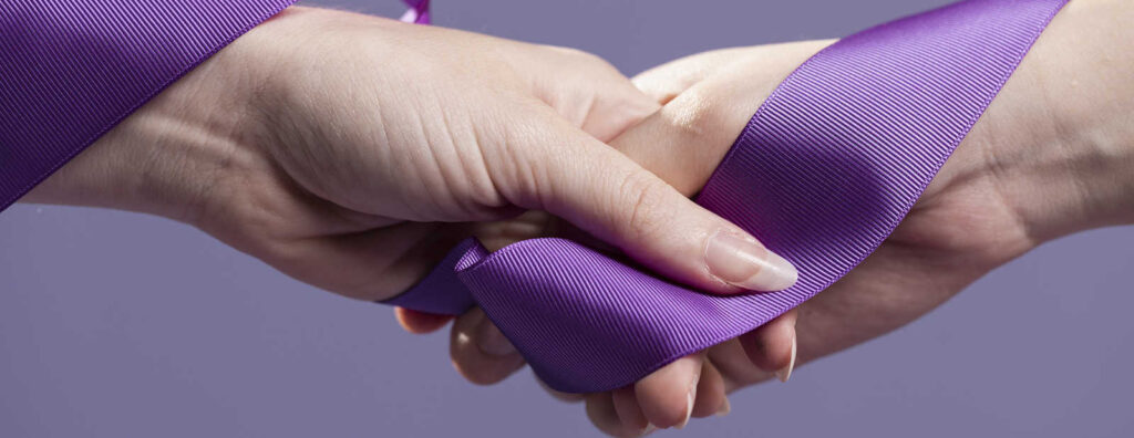 Manos entrelazadas sosteniendo un lazo morado, símbolo de concienciación por el Día Mundial del Lupus.