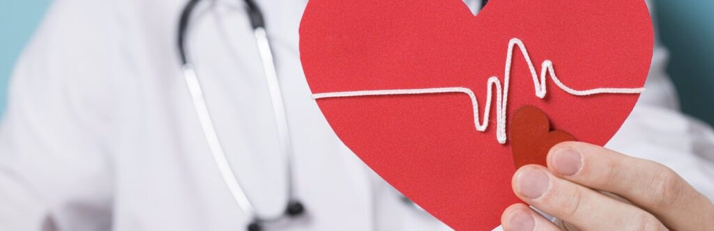 Médico sosteniendo un corazón rojo con un electrocardiograma, representando la concienciación sobre el Día Mundial de la Hipertensión.