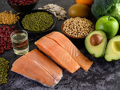 Alimentos ricos en nutrientes como salmón, aguacate, legumbres y vegetales verdes, dispuestos sobre una mesa. Destaca el papel de una alimentación balanceada en el fortalecimiento del sistema inmune durante el tratamiento contra el cáncer.