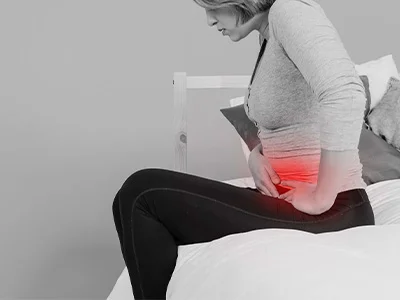 Mujer se sostiene el abdomen por un dolor, que se destaca con una zona roja sobre la foto en blanco y negro.