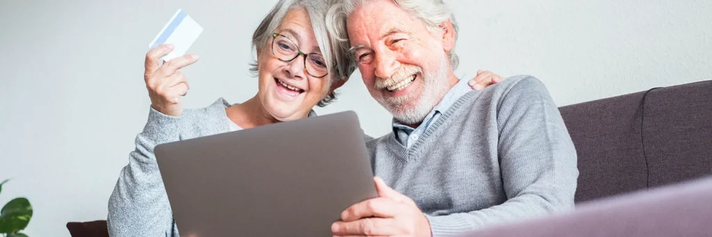 Pareja mayor feliz realizando una compra online con tarjeta en Cofar Salud durante el Cyber Day.