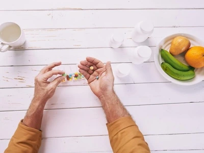 Persona tomando suplementos o medicamentos junto a frutas frescas y agua, representando un estilo de vida saludable para el corazón.