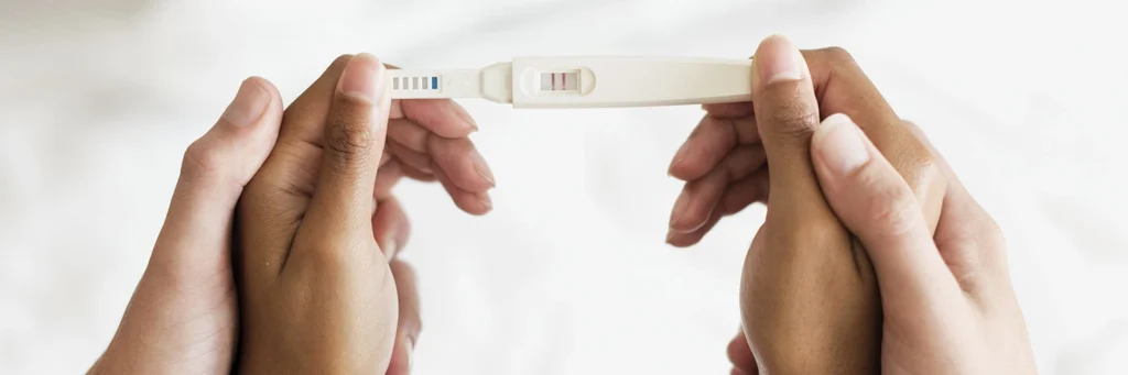 Manos de una pareja abrazada, sosteniendo un test de embarazo positivo