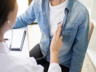 Doctora revisando el corazón de un paciente con un estetoscopio durante un control médico.