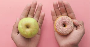 Manos sosteniendo una manzada y una dona, haciendo referencia al manejo alimenticio de la diabetes
