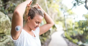Mujer con monitor de glucosa en el brazo mientras se recoje el cabello, haciendo referencia a mitos sobre la diabetes