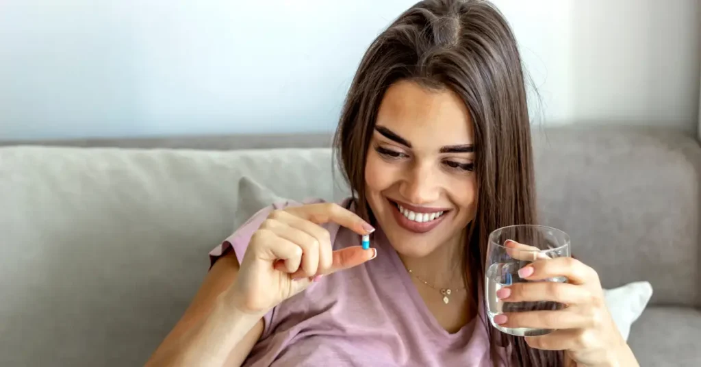Mujer sonriendo mientras sostienen una cápsula blanda de suplemento vitaminico, haciendo referencia a vitaminas que no pueden faltar