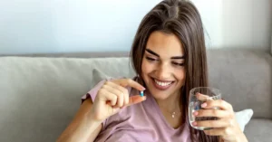 Mujer sonriendo mientras sostienen una cápsula blanda de suplemento vitaminico, haciendo referencia a vitaminas que no pueden faltar