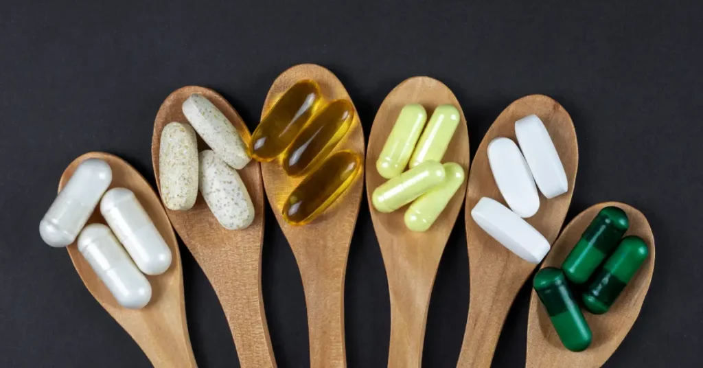 Cucharas de madera con diferentes capsulas de suplementos vitaminicos y minerales, haciendo referencia a minerales y vitaminas