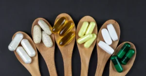 Cucharas de madera con diferentes capsulas de suplementos vitaminicos y minerales, haciendo referencia a minerales y vitaminas
