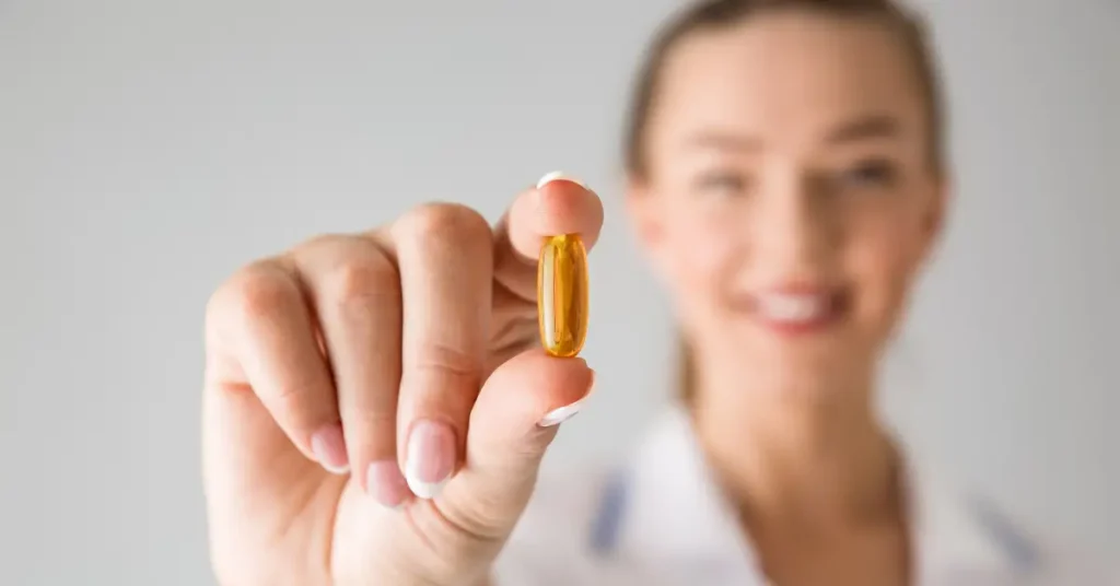 Mujer sosteniendo una capsula blanda de vitaminas en primer plano, haciendo refrencia vitaminas esenciales