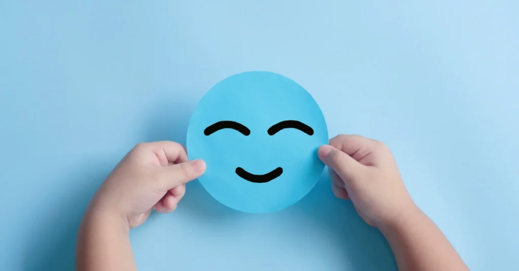 Cara de papel sonriente sujeta por las manos de un niño con fondo azul claro