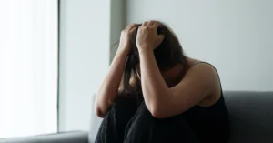 Mujer sentada en el sofá muy estresada con las manos en la cabeza tapandose la cara. haciendo alusión al artículo El vinculo secreto como el estrés afecta tu corazón y tu cuerpo