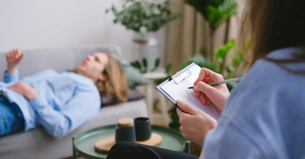 Hombre acostado en el diván mientras su teraéuta toma notas, haciendo alución a los 7 factores que afectan tu salud mental