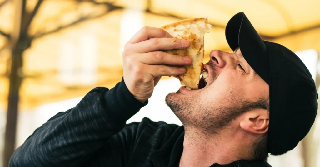 Hombre comiendo una pizza, haciendo referencia al artículo 4 Pasos para Vencer el Hambre Emocional: Recobra tu Confianza al Comer