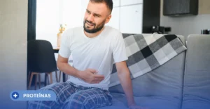Hombre sentado en un sofá tocándose el estómago con expresión de dolor abdominal, evidenciando la necesidad de buscar una proteína en polvo para intolerantes a la lactosa para evitar molestias digestivas.