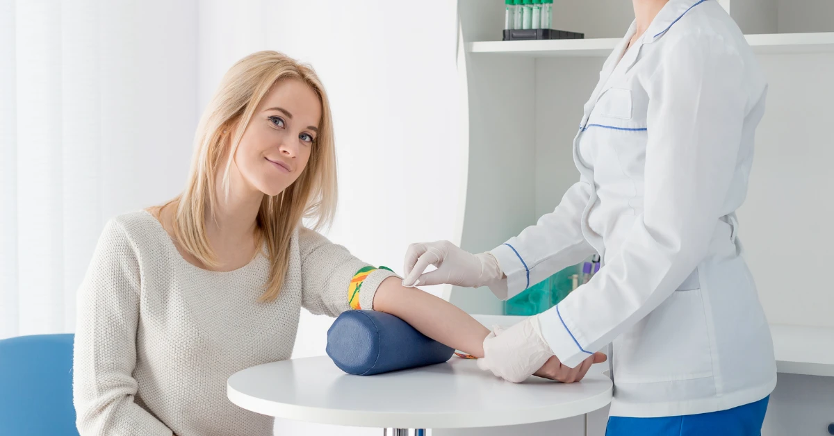 Mujer joven sonriendo en un laboratorio clínico mientras una enfermera profesional se prepara para realizar la extracción de sangre necesaria para el test de HOMA.