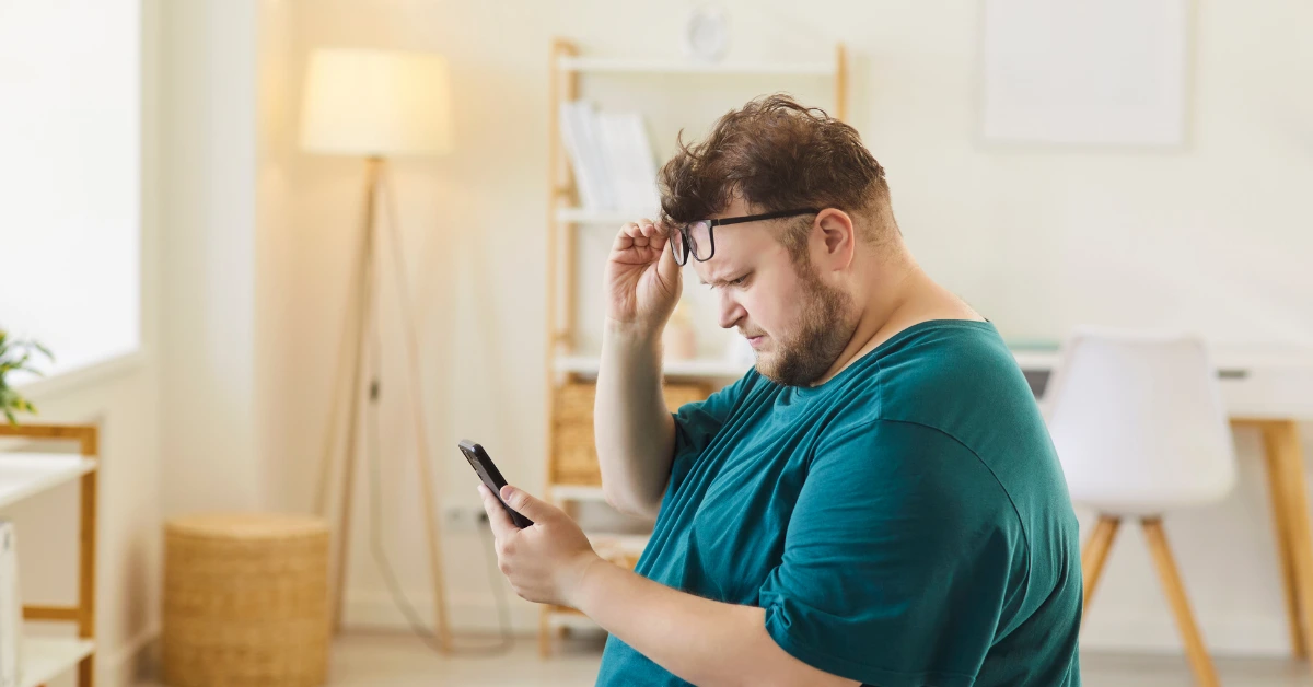 Hombre adulto mirando su teléfono móvil con expresión de preocupación, leyendo información sobre qué significa ser resistente a la insulina y los pasos iniciales para acudir al médico especialista.