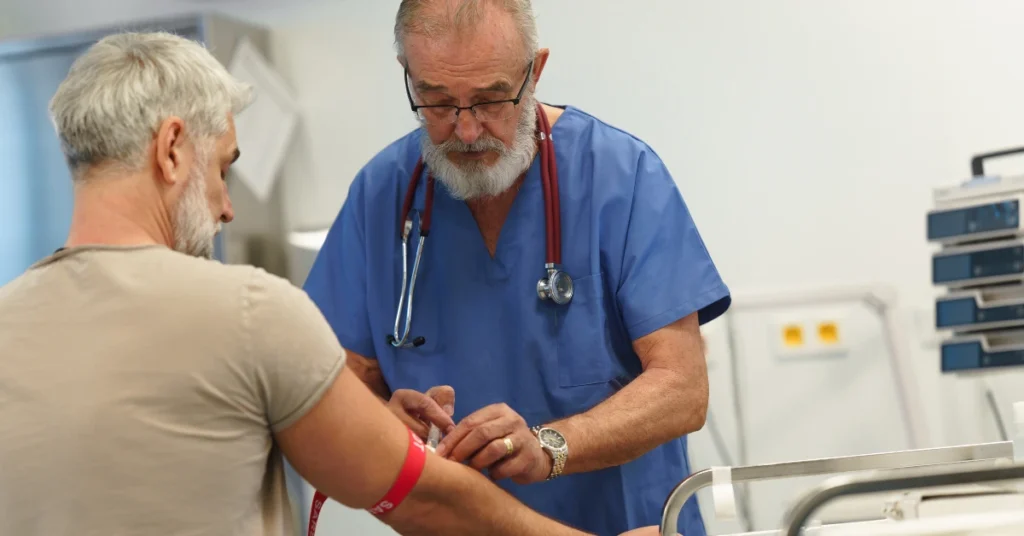 Profesional médico con uniforme azul y estetoscopio realiza una extracción de sangre en el brazo de un paciente para medir la glucemia basal en una clínica.